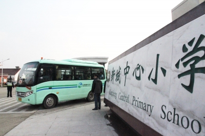 镇村公交校车按顺序驶出校园送学生回家。